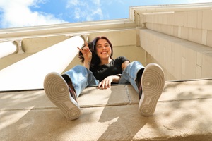 A USD Student posing with a peace sign sitting on a short building edge.