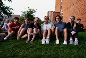 A group of students sitting and smiling outside of the Coyote Village volleyball court.