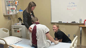 Two health science students working with simulation patient in medical room