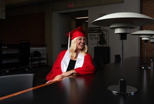 female student sitting at a table in her cap and gown