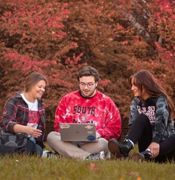 Three Students Sitting in the Grass on Laptop
