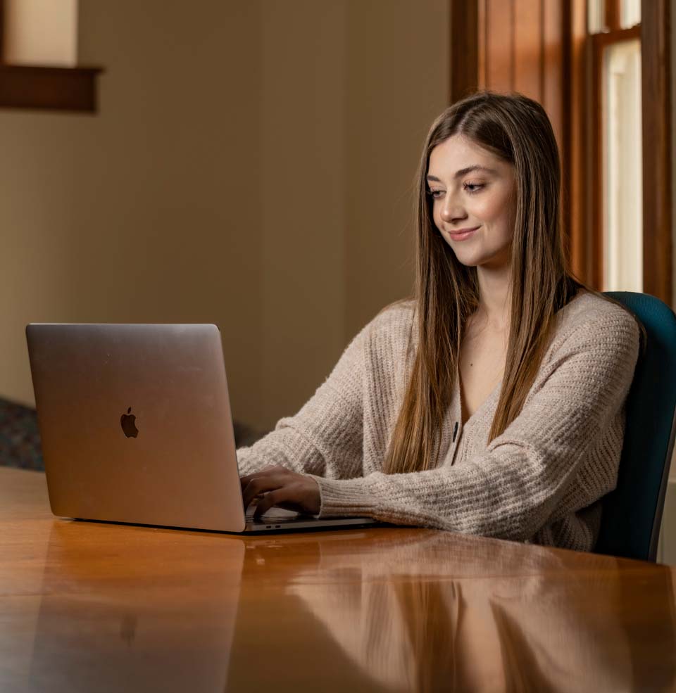 Female Student Sitting at Table with Laptop.