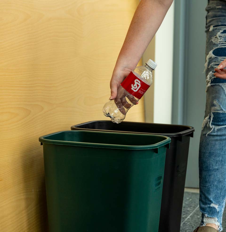 Someone throwing a plastic bottle into a recycling bin