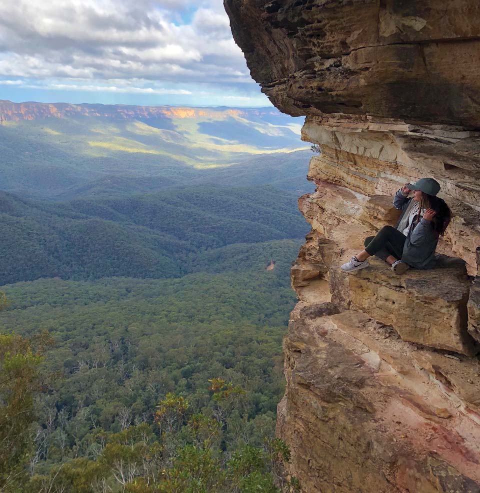 A student sitting on a ledge on the side of a cliff or mountain