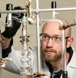 Student wearing gloves and lab coat working with clear pipes and tubes.