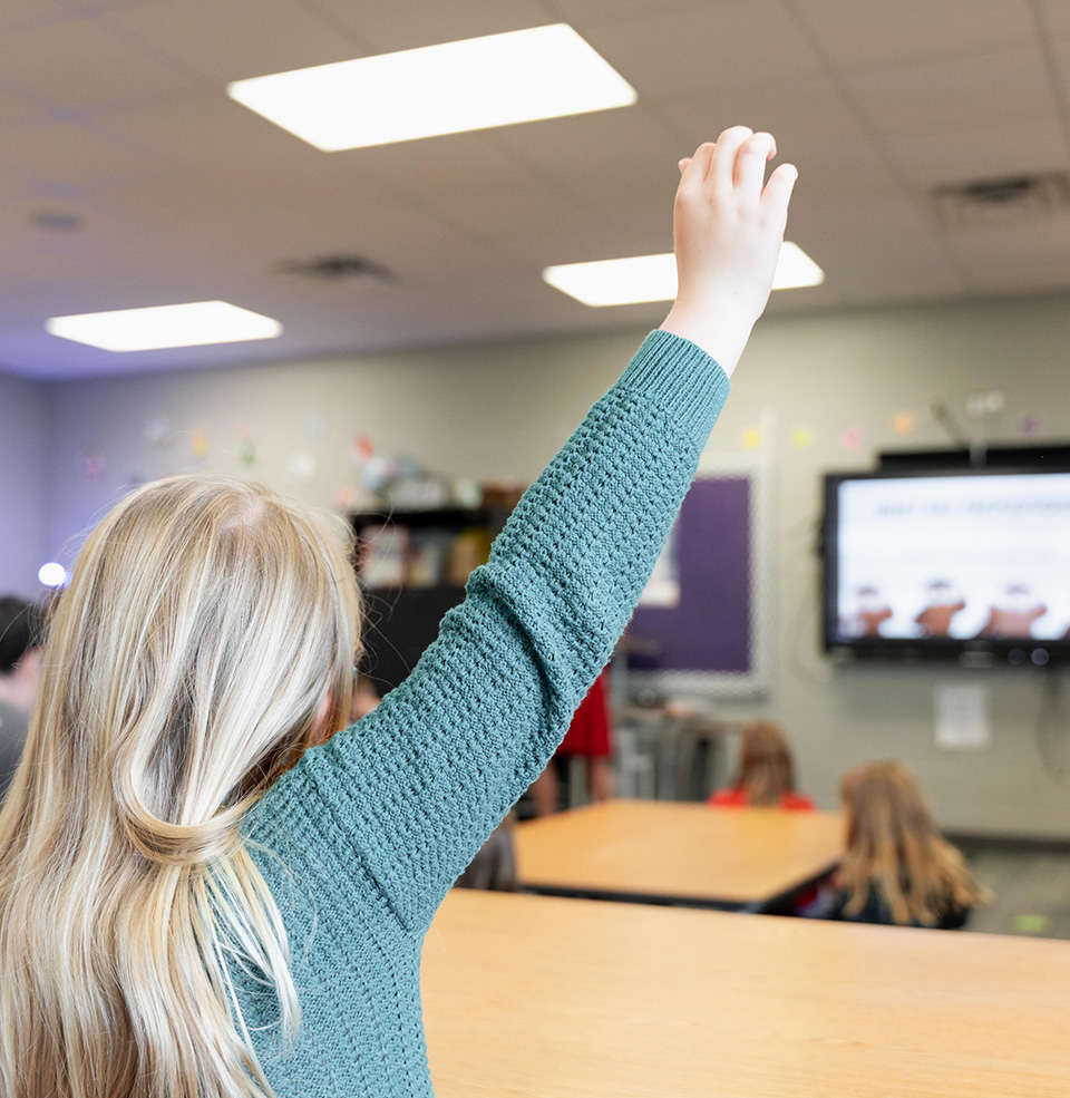 Child raising hand in classroom.