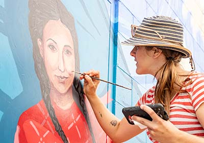 Student painting a mural on building.