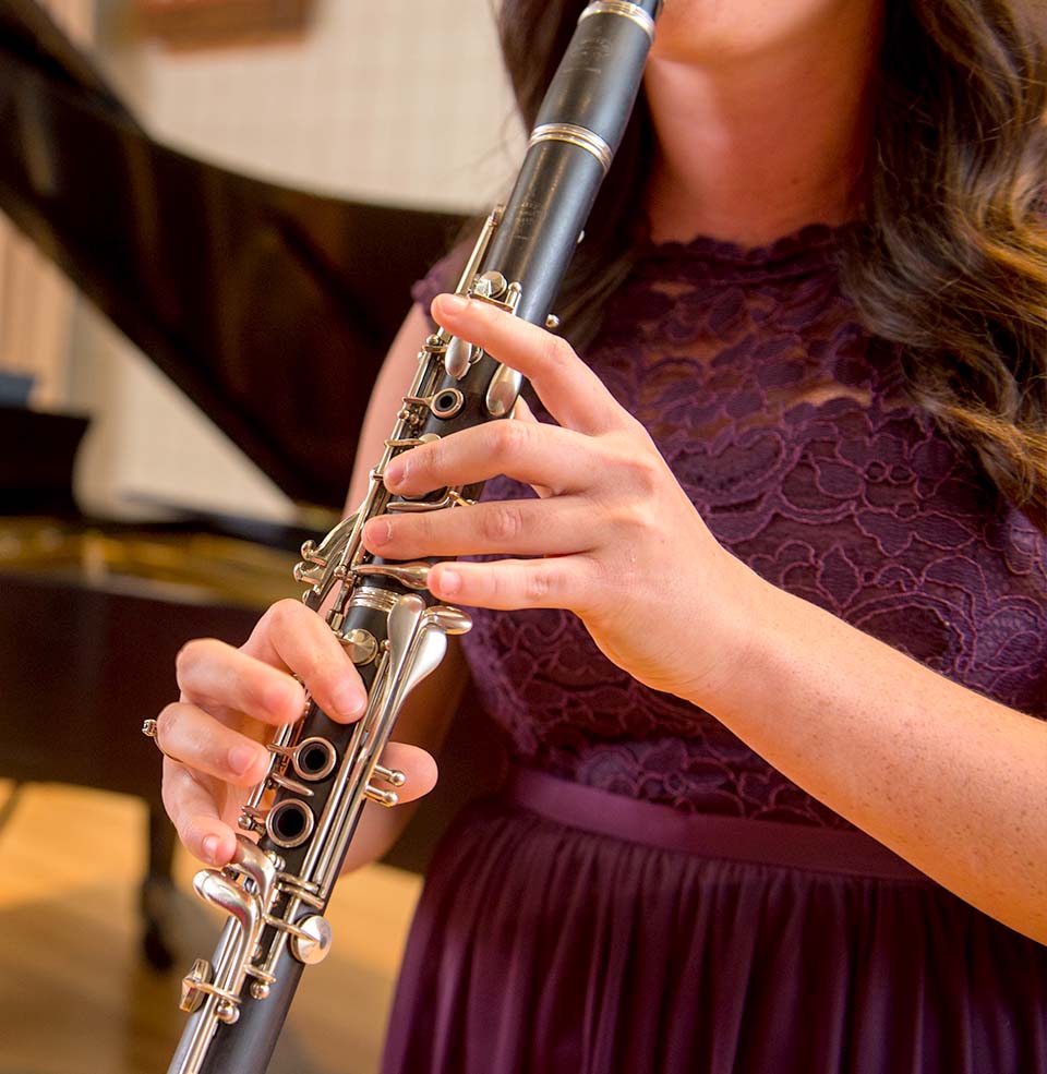 Student playing a clarinet with piano in the background.