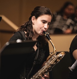 A USD student playing a saxophone on stage with other performers.