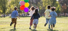 Five children holding balloons running in a field.