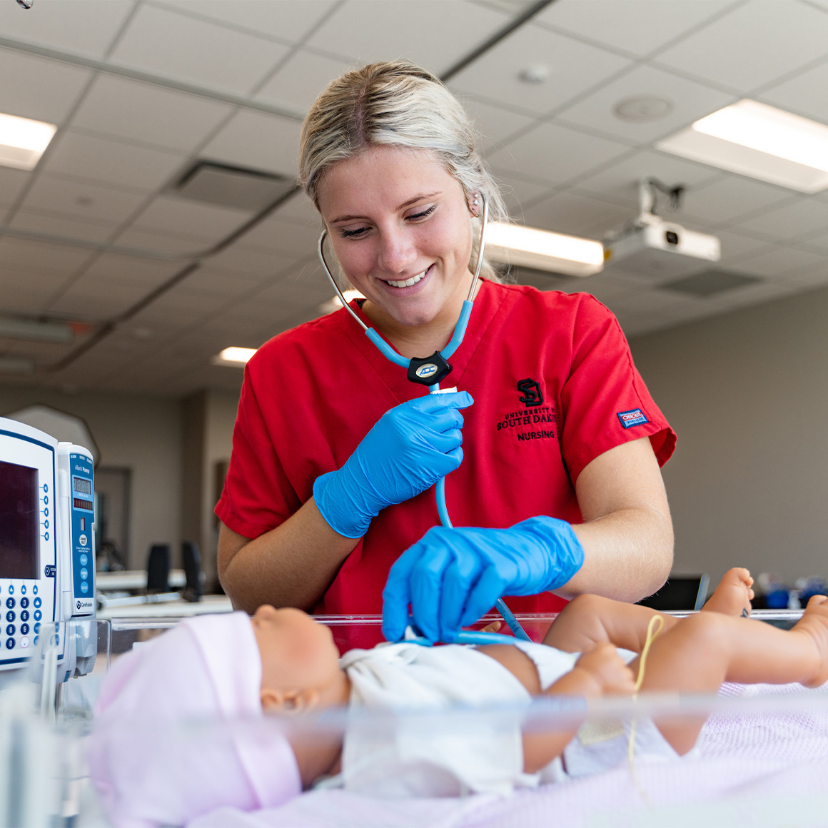 A Health sciences student smiling and working on a fake baby model.