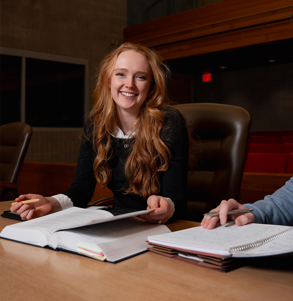 Law student sitting in formal clothes at a desk with a textbook in front of her and smiling.
