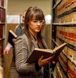 Female Law Student Reading a Book in the Aisle of the Library.
