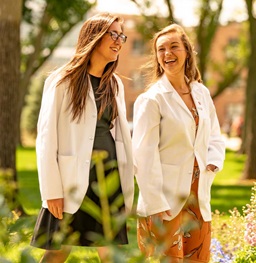 Two Female Student in White Lab Coats Walking Outdoors