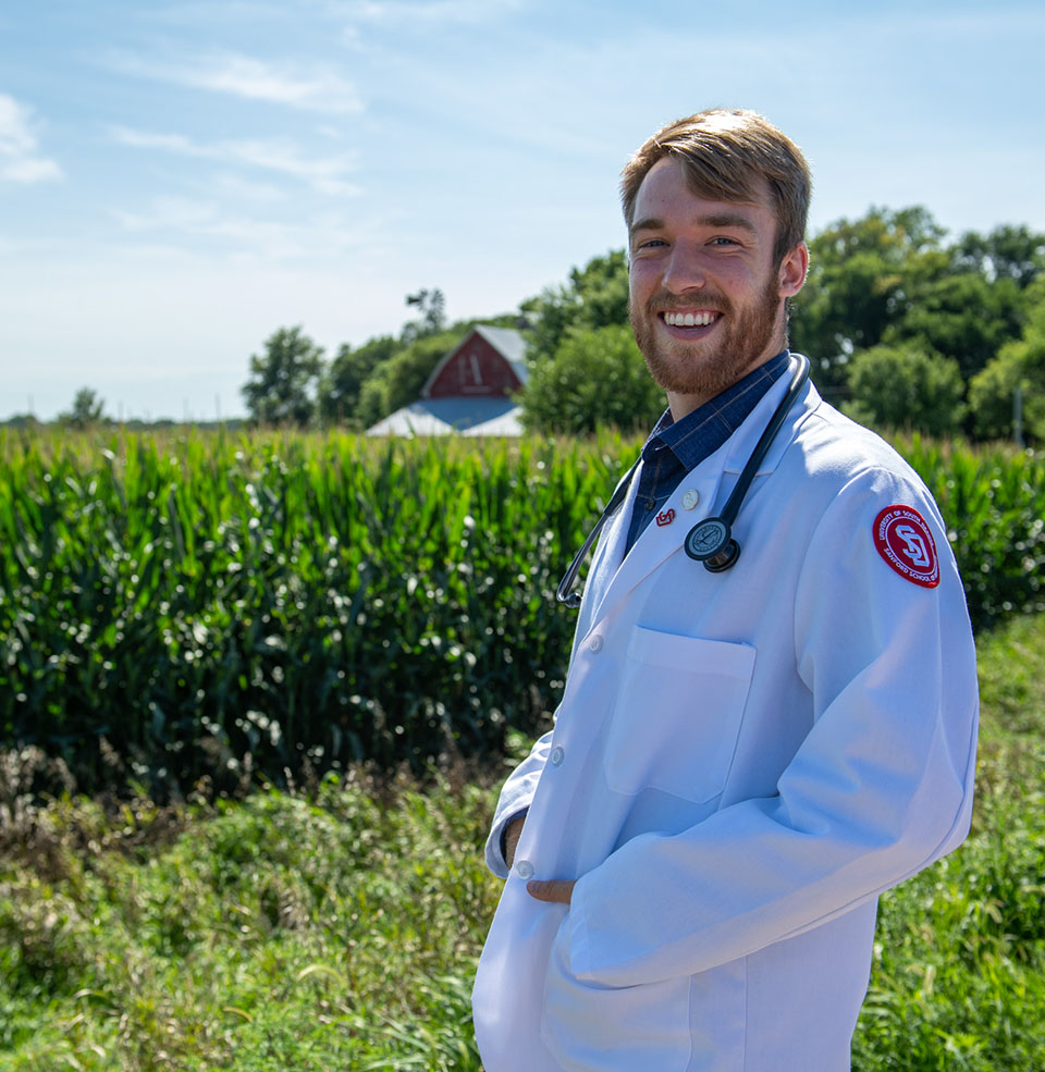 Medical student in a white coat standing near a corn field