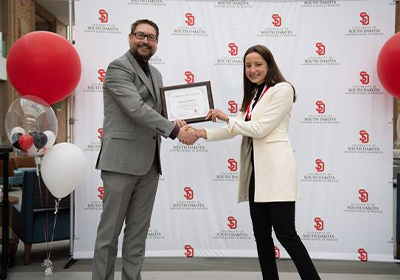Two medical school faculty shaking hands, and exchanging an award.
