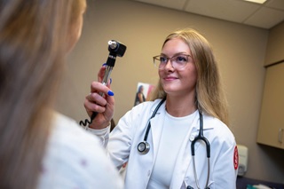 A med student smiling and holding a handheld medical tool for eye care.