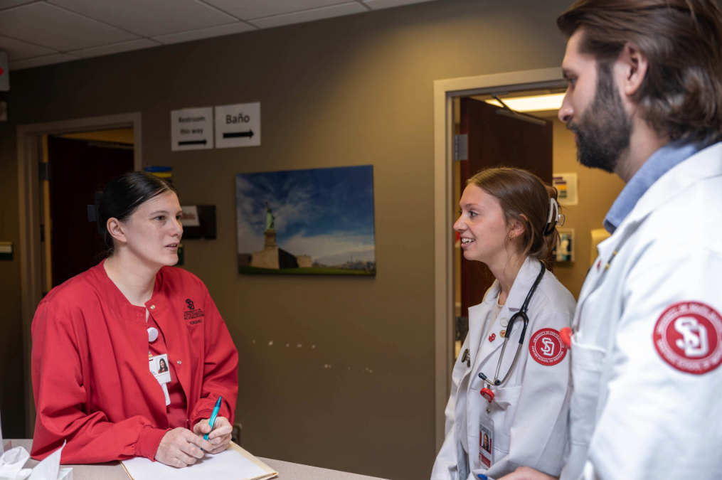 Two med students talking to a faculty member at the Coyote Clinic front desk.