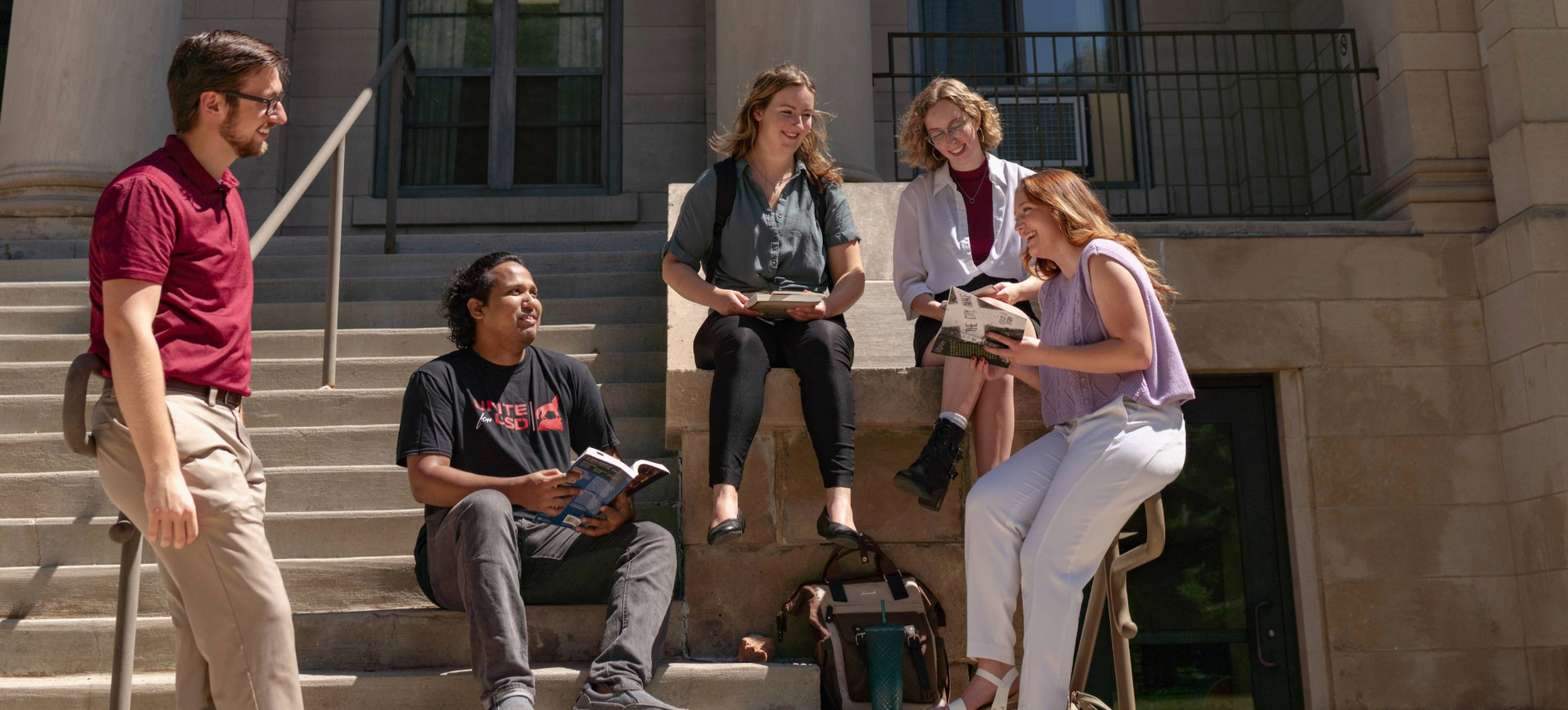 English students sitting on the arts and sciences building stairs and smiling.