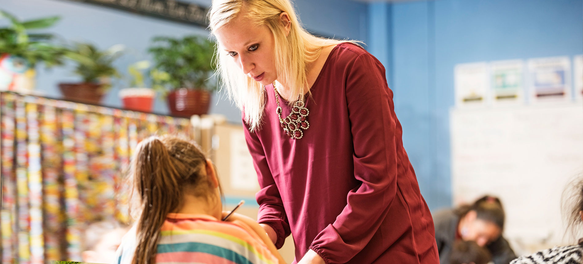 A teacher in a classroom assisting a young student with work 