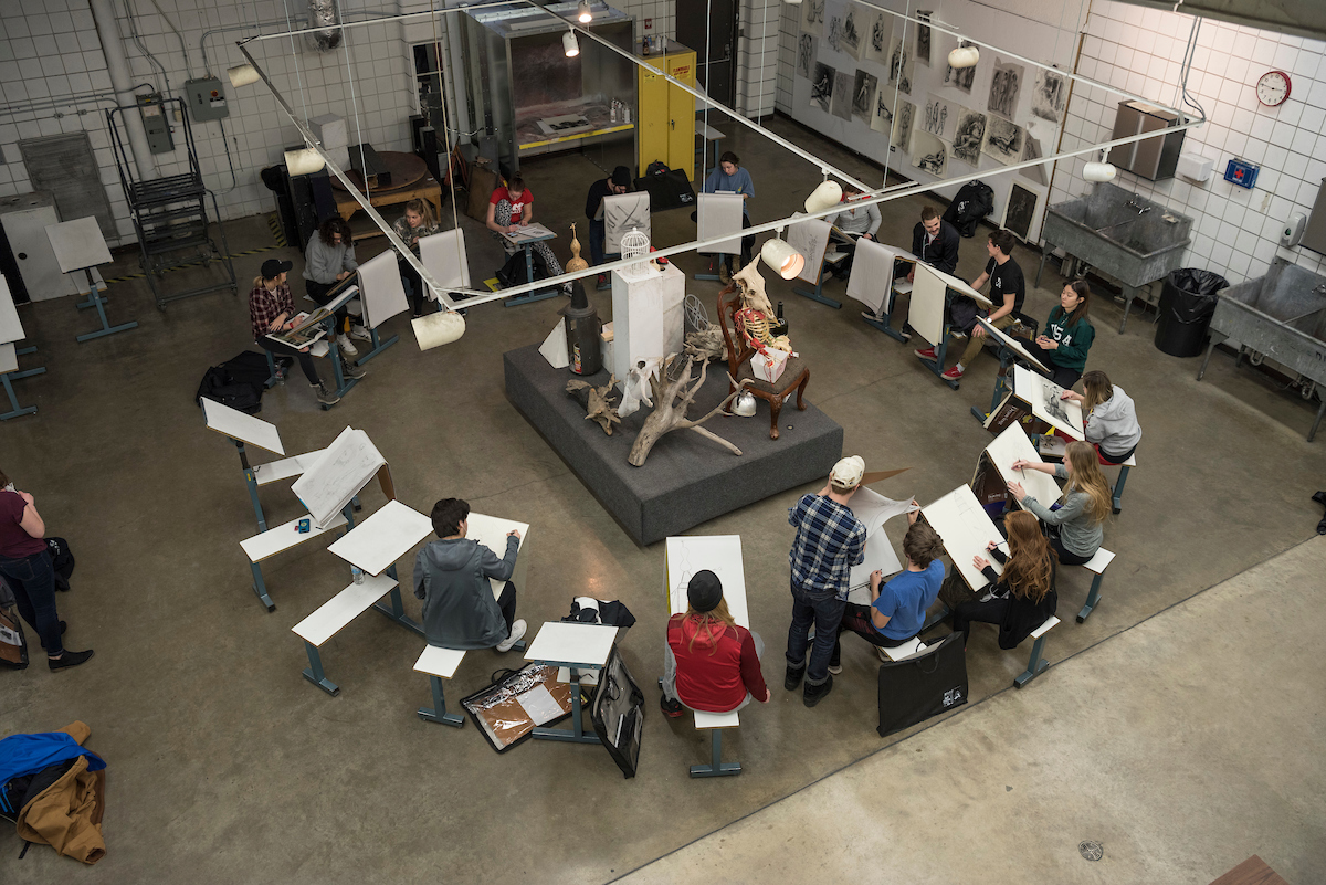 Art class with students circled up with sketch pads around a scene in the middle of the circle