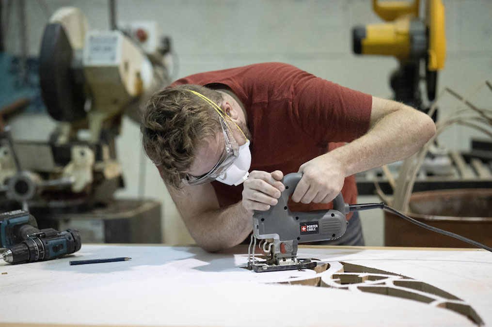 Student using a jigsaw to cut out a design in a large wooden board