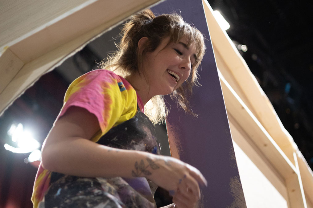 Student wearing a builders apron and having fun working on building the scene props 