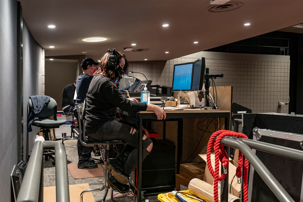 Students wearing headphones and sitting at the boards and computers in the director's booth