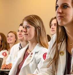 Students in White Lab Coats Listening in Classroom.