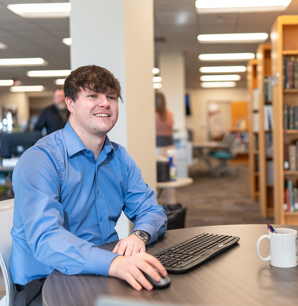Student on a computer in the library holding a mouse.