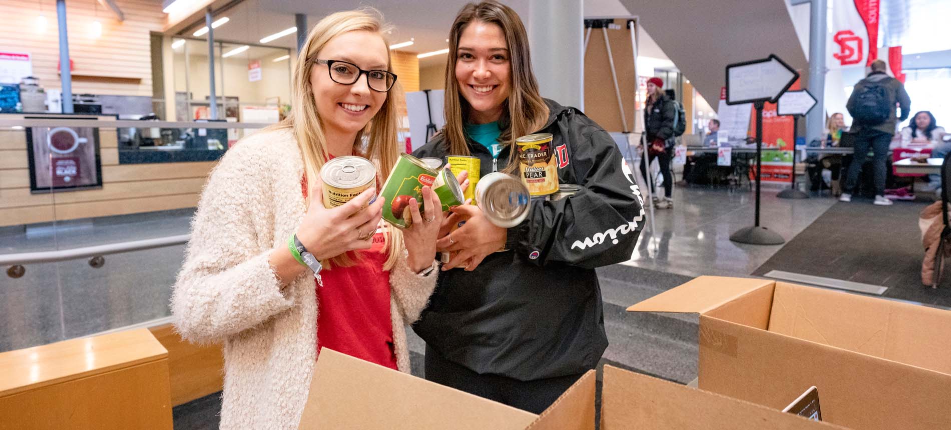 Two Female Students Helping at a Food Drive.