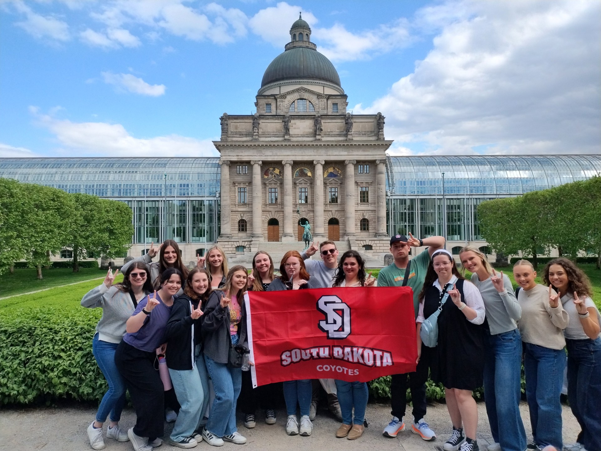 Students out front of  campus building grouped up with a USD banner for a group photo