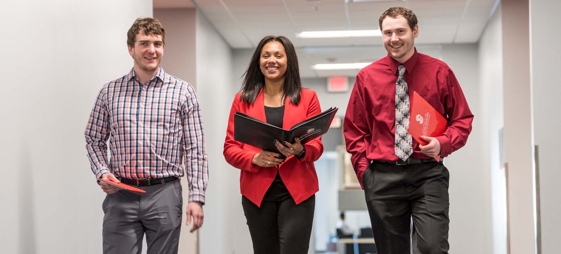 Three Students in Professional Wear Walking Down Hallway.