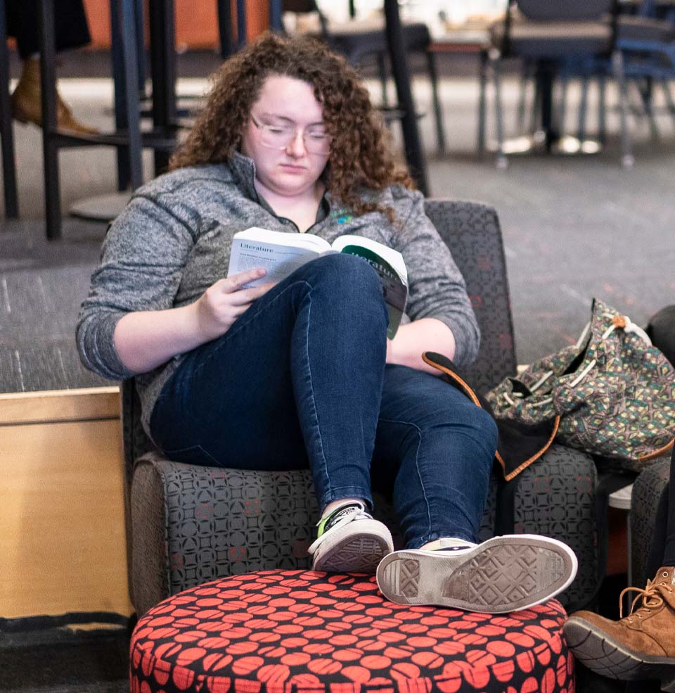 Female Student Sitting in a Chair Reading a Book.