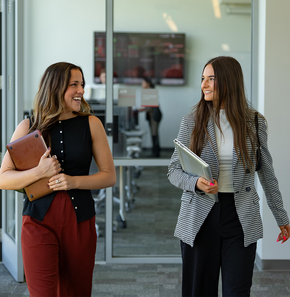 Two students in business clothing walking through a building on campus with books in their hands.