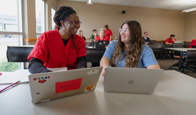 Two students typing on their laptops and talking.