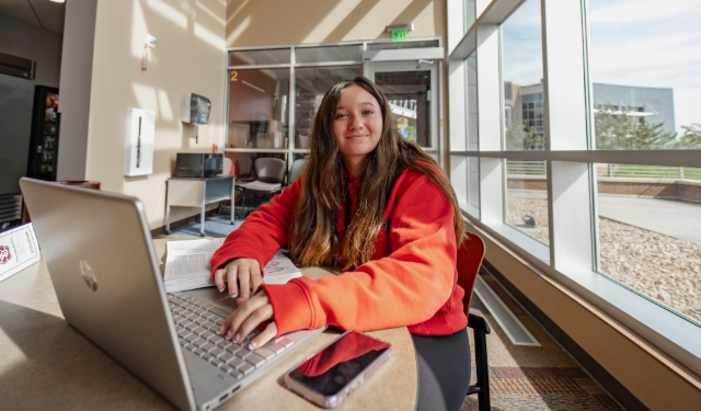 A student at the Sioux Falls campus smiling and typing on her laptop.
