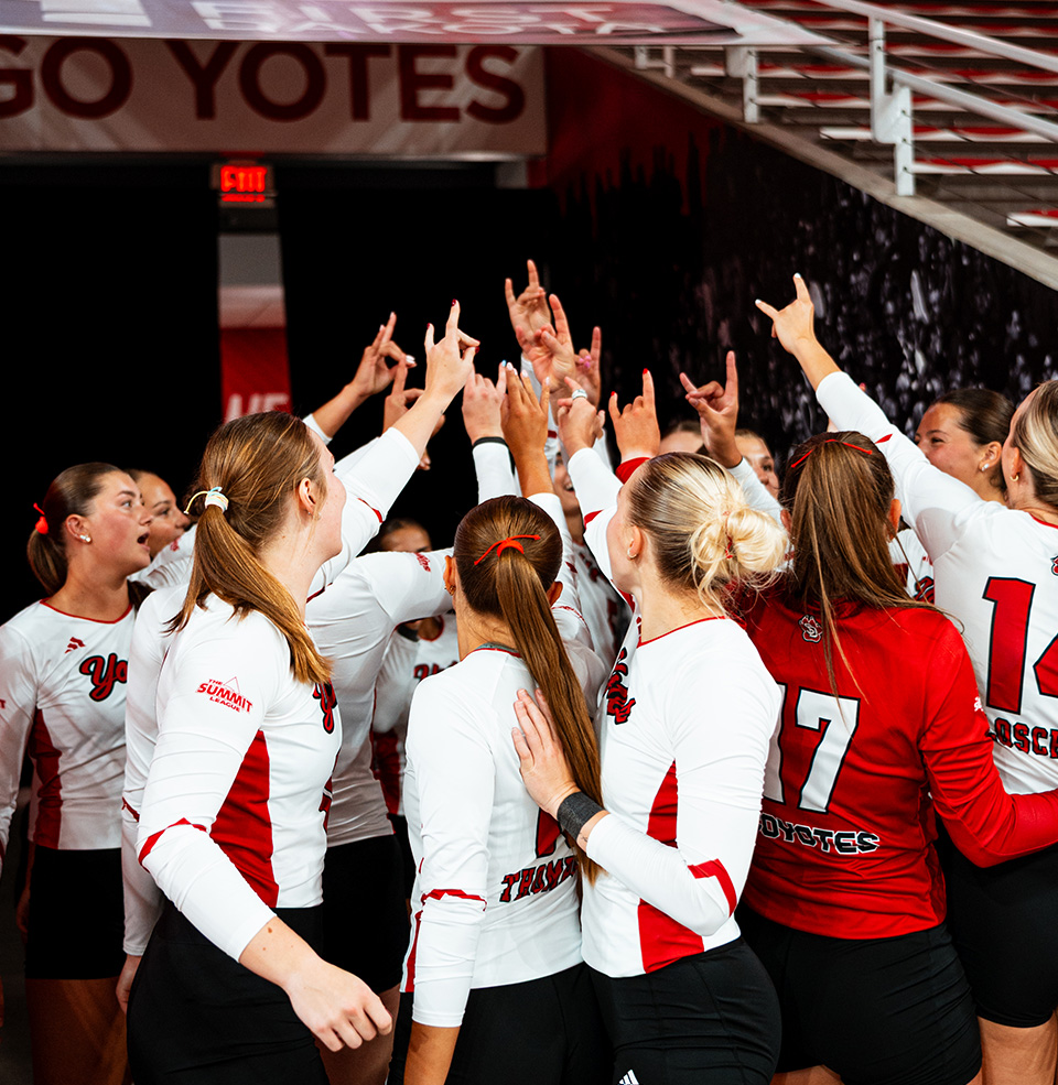 USD Coyote Volleyball team in a huddle with Coyote hands in the air