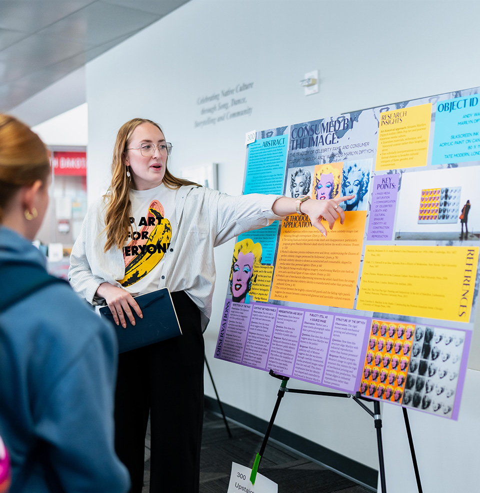 A student standing in front of a board that shows their research project about pop art