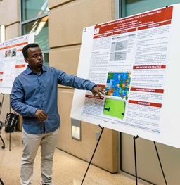 Male Student Presenting his Research at a Poster Session Event