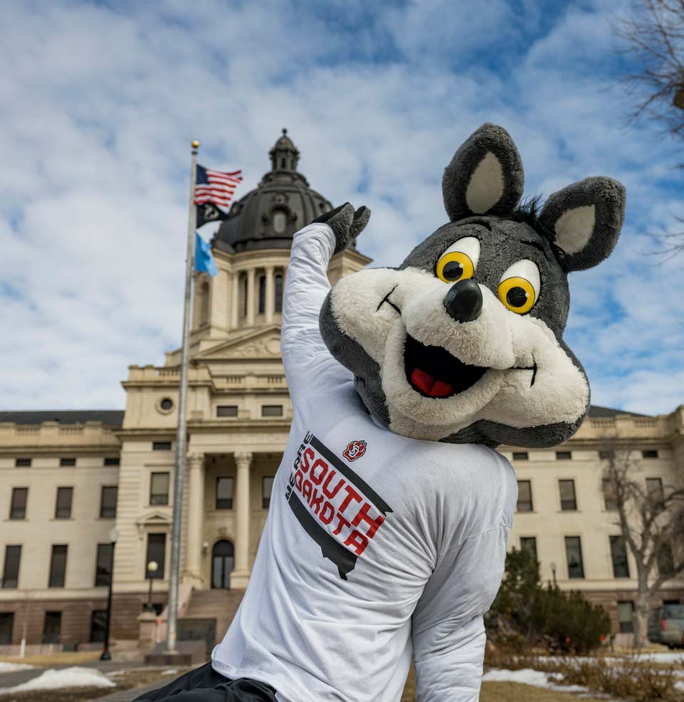 Charlie Coyote posing in front of the South Dakota Capitol.