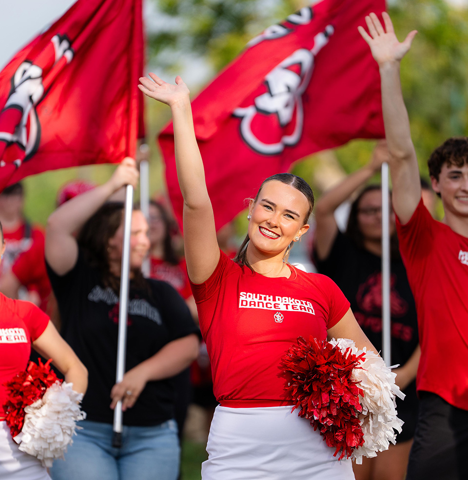 USD Dancer smiling at Presidents Picnic in front of USD Paw Print flags.