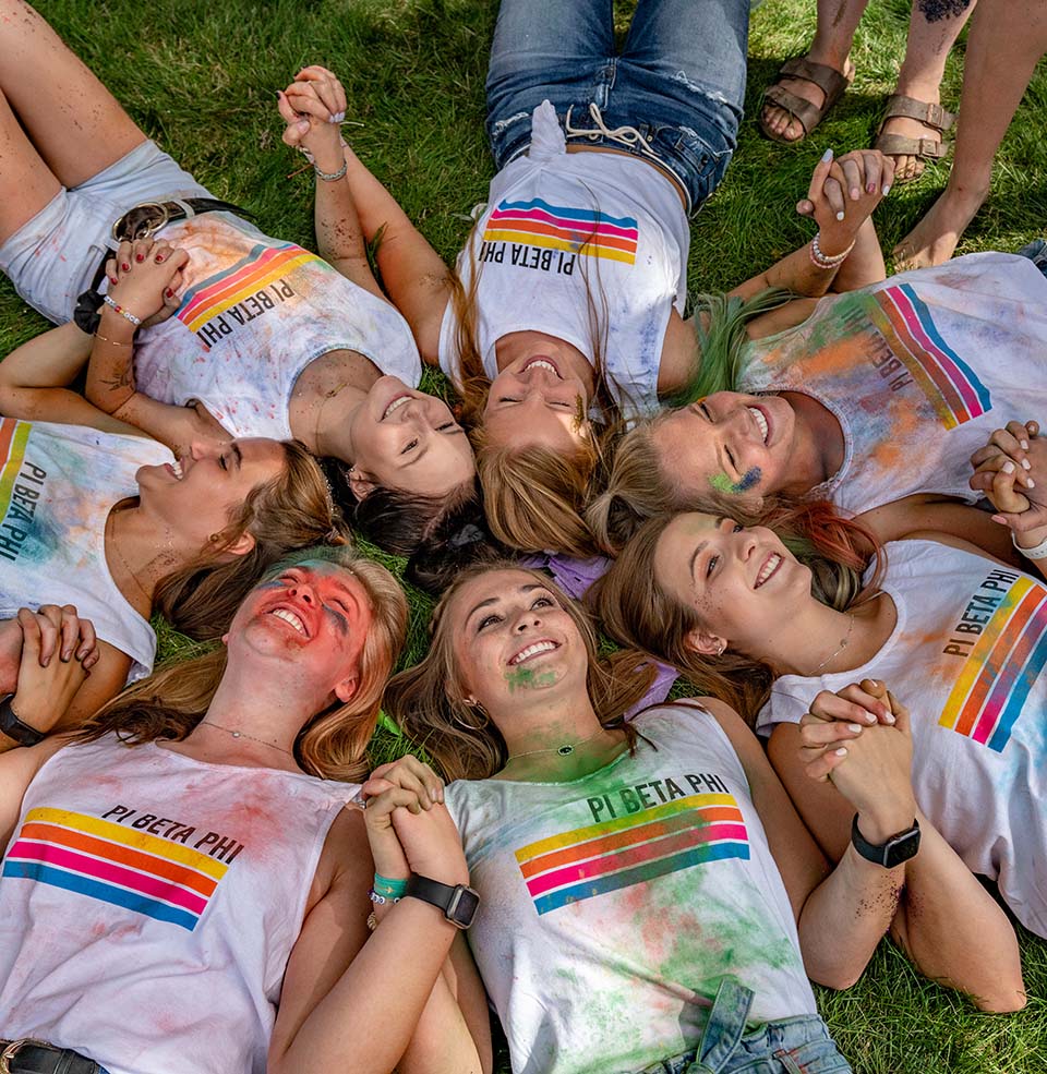 sorority girls laying in circle holding hands in the grass