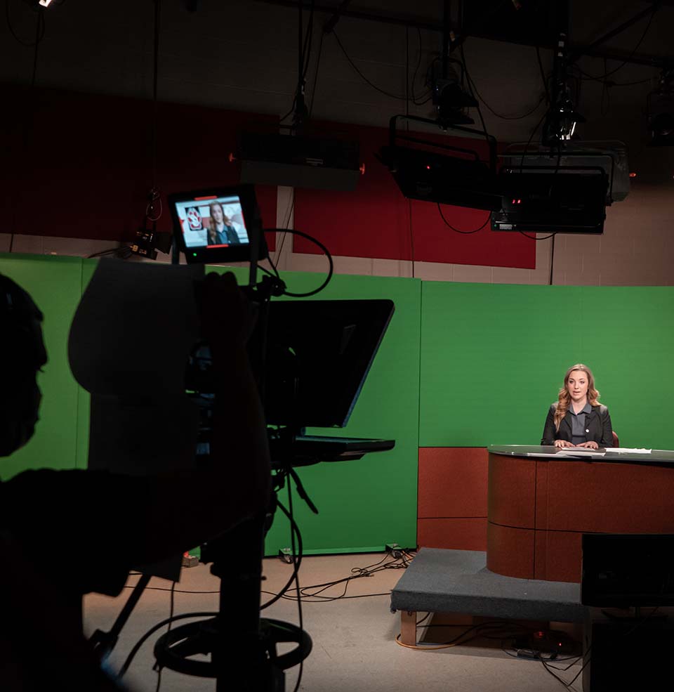 Student behind the anchor's desk in a Coyote News broadcast