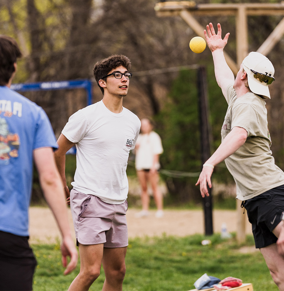 Fraternity brothers playing an outdoor game with a yellow ball.
