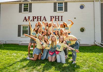 Alpha Phi girls posing together in front of their sorority house.