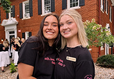 Two sorority sisters smiling in front of their house during rush week.