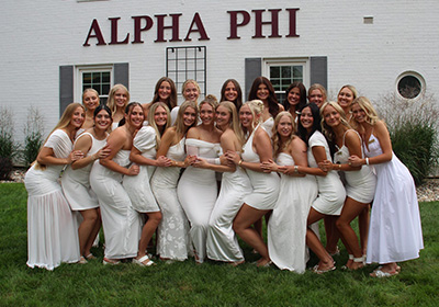 Group of sorority sisters wearing white dresses in front of USD's Alpha Phi house.