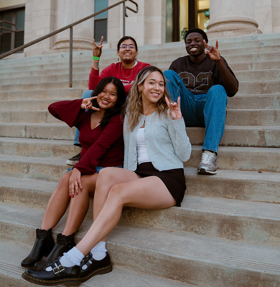 Group of students on the steps of a campus building showing Yote hands