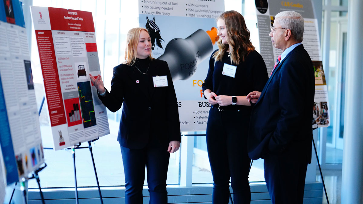 A student presents a poster to two people.